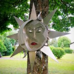 Skulptur "Sonne, Mond und Sterne" vor einem Baum